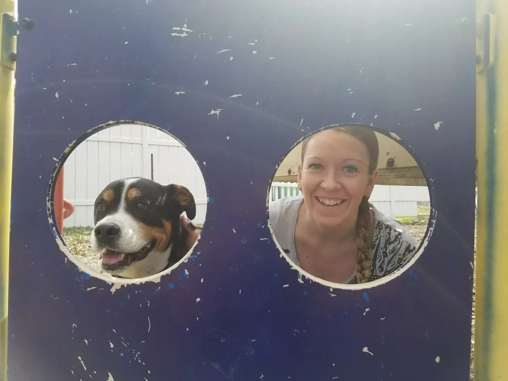 A woman and a dog peeking through round holes in a blue play structure.