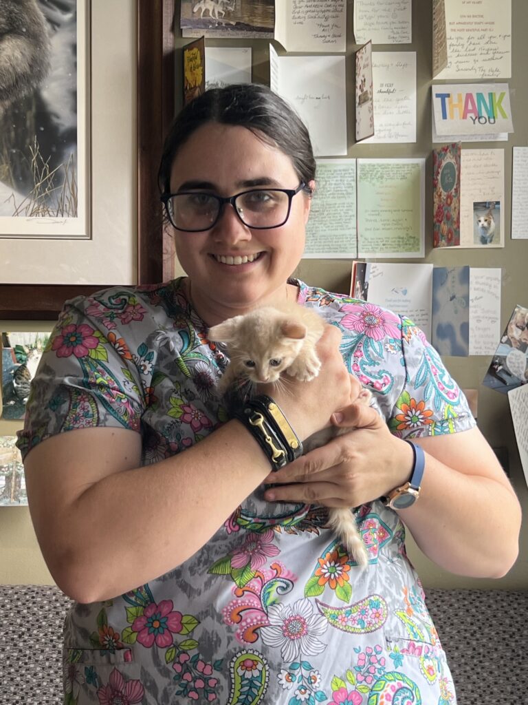 Woman smiling and holding a small, light-colored kitten.