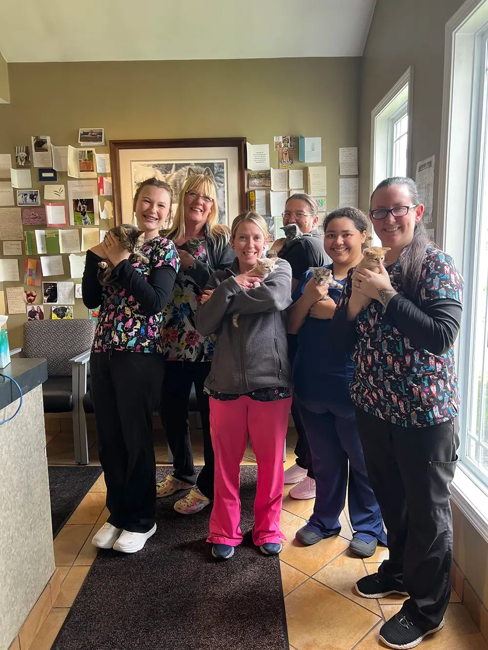 Group of five women in scrubs, each holding a kitten, smiling in a room.