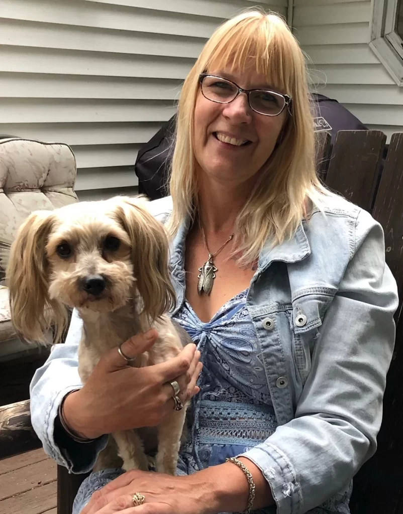 A smiling woman holding a small dog on a porch.